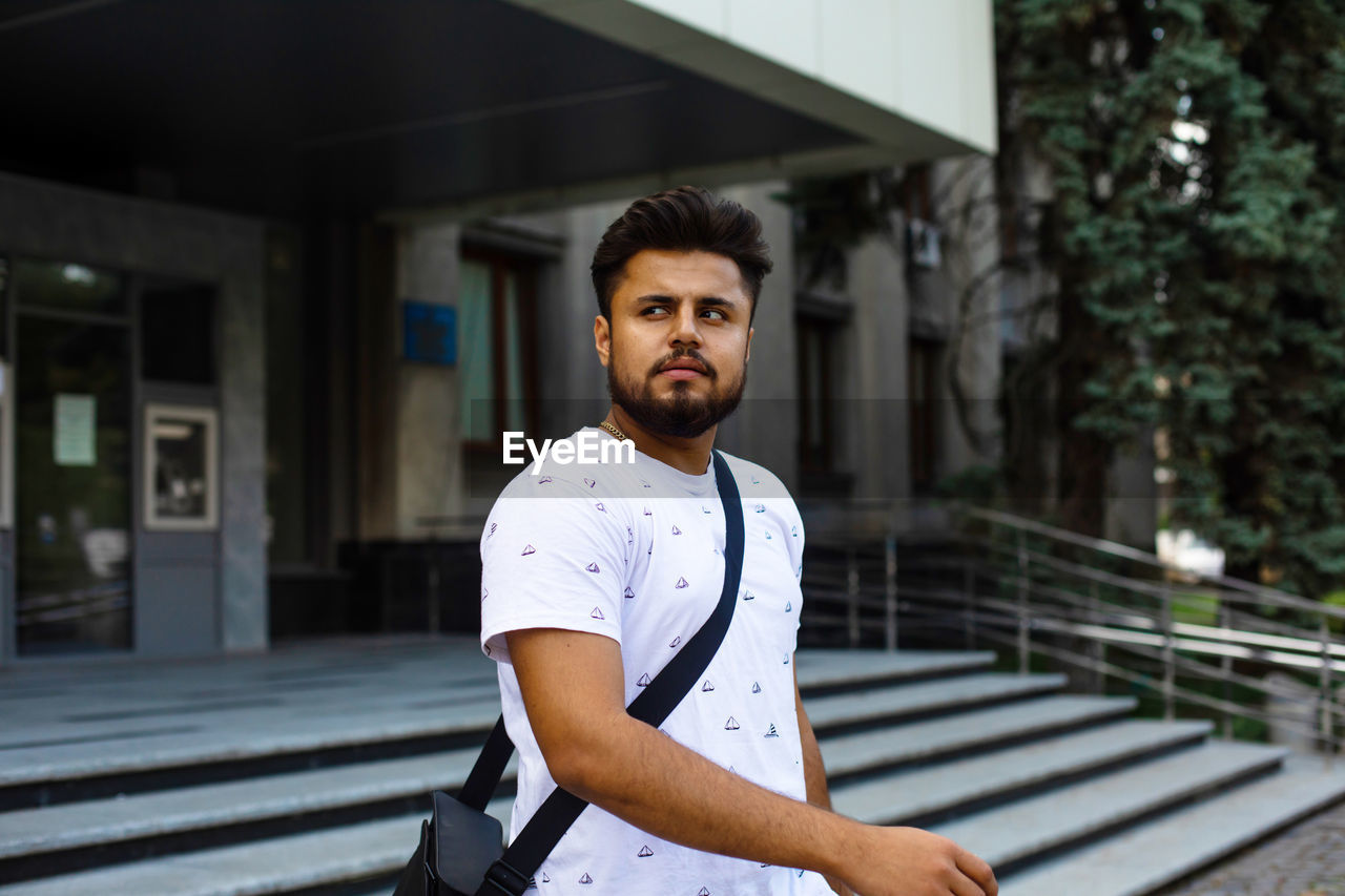 portrait of young man looking away while standing outdoors