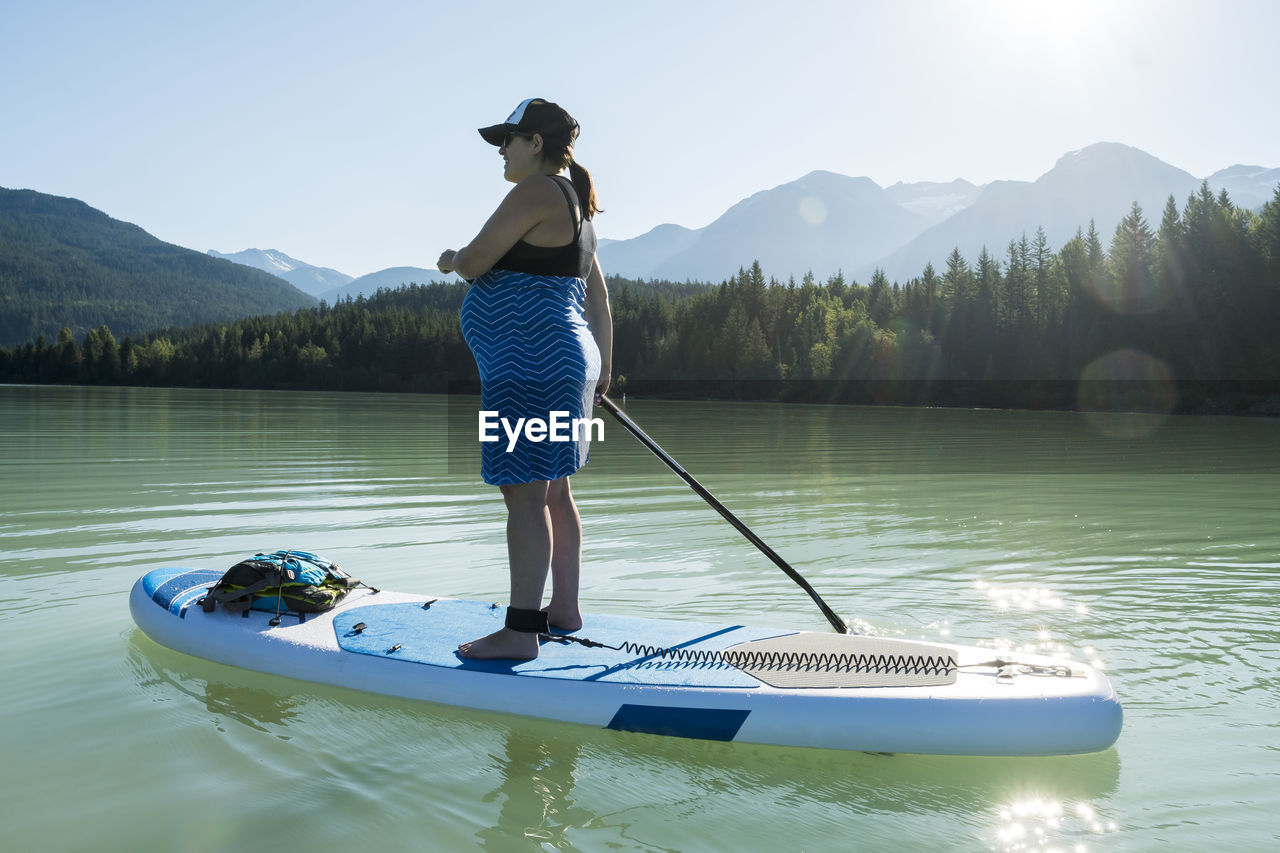 Pregnant female riding sup board on mountain lake