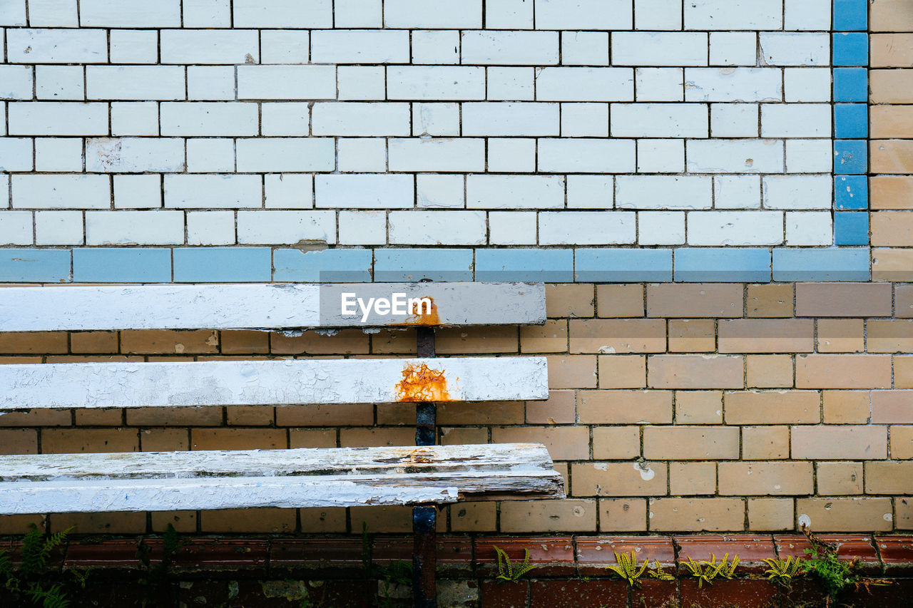 A worn and weathered wooden bench against a colorful tiled wall