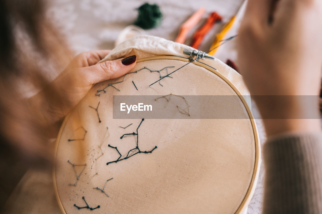 Side view of crop female with hoop and threads embroidering star constellations while sitting at table in light workshop