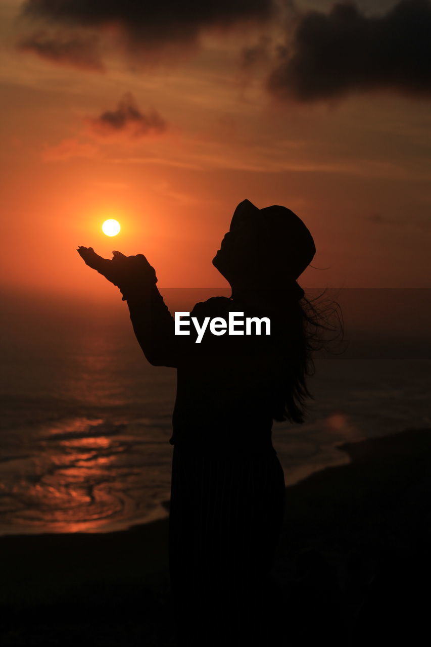 SILHOUETTE MAN STANDING ON BEACH AGAINST ORANGE SKY