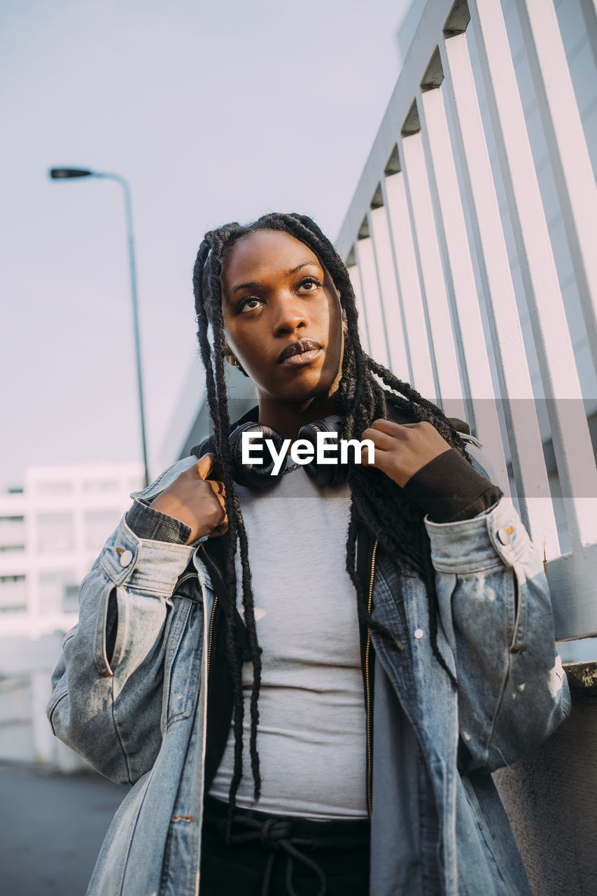 Young woman wearing denim jacket by fence