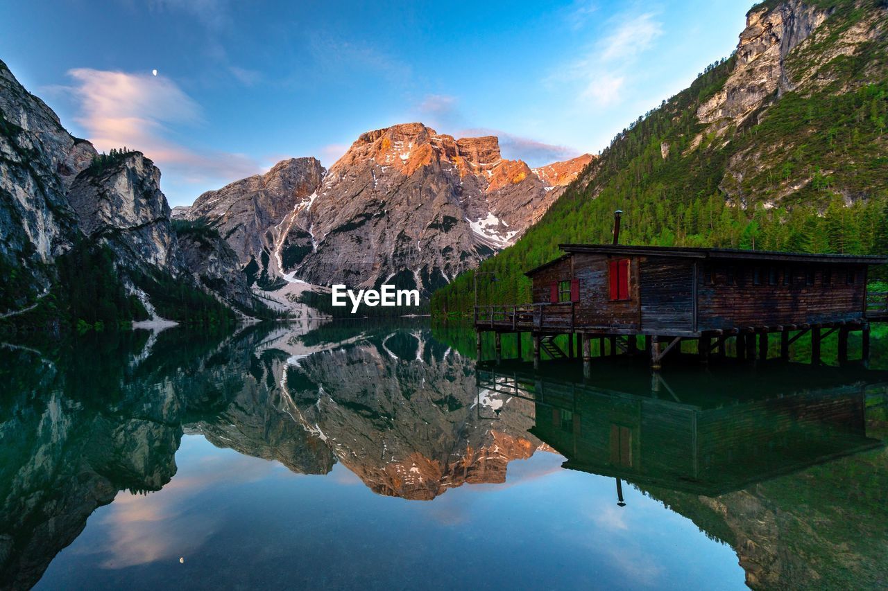 Scenic view of calm lake with stilt house and mountains reflection