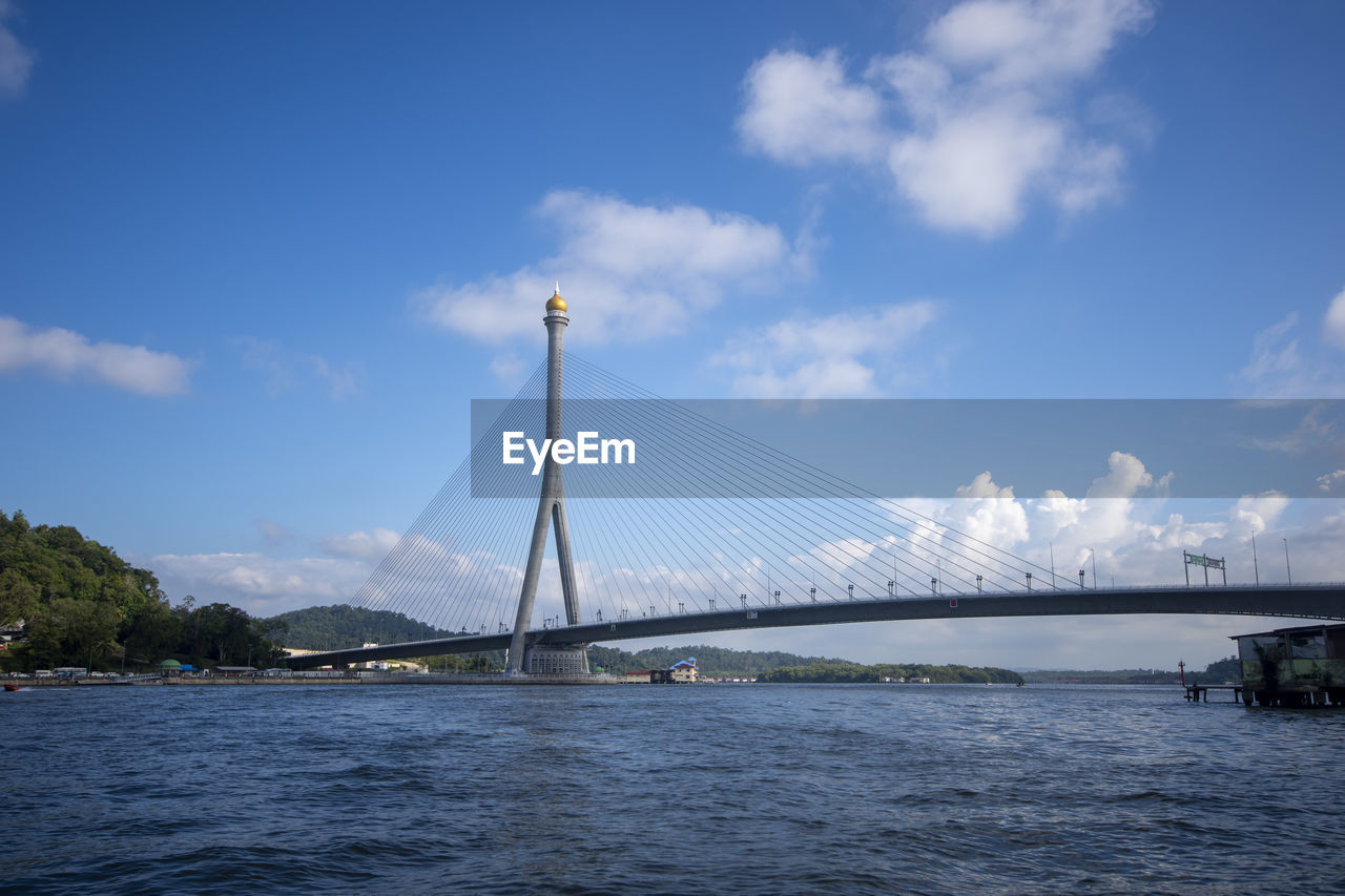 View of suspension bridge over river against cloudy sky