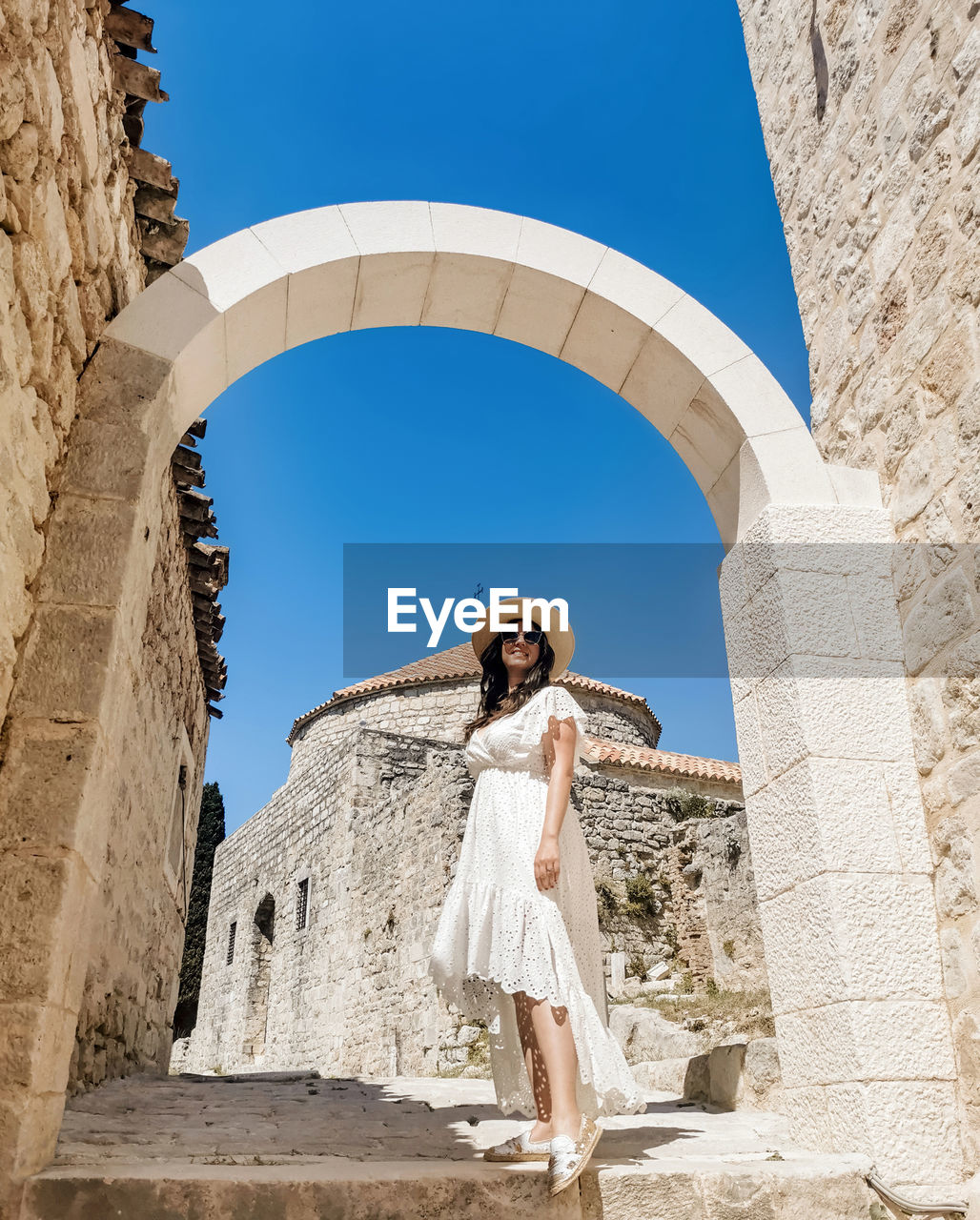 Low angle full length image of young woman wearing white dress standing in stone street in old town.