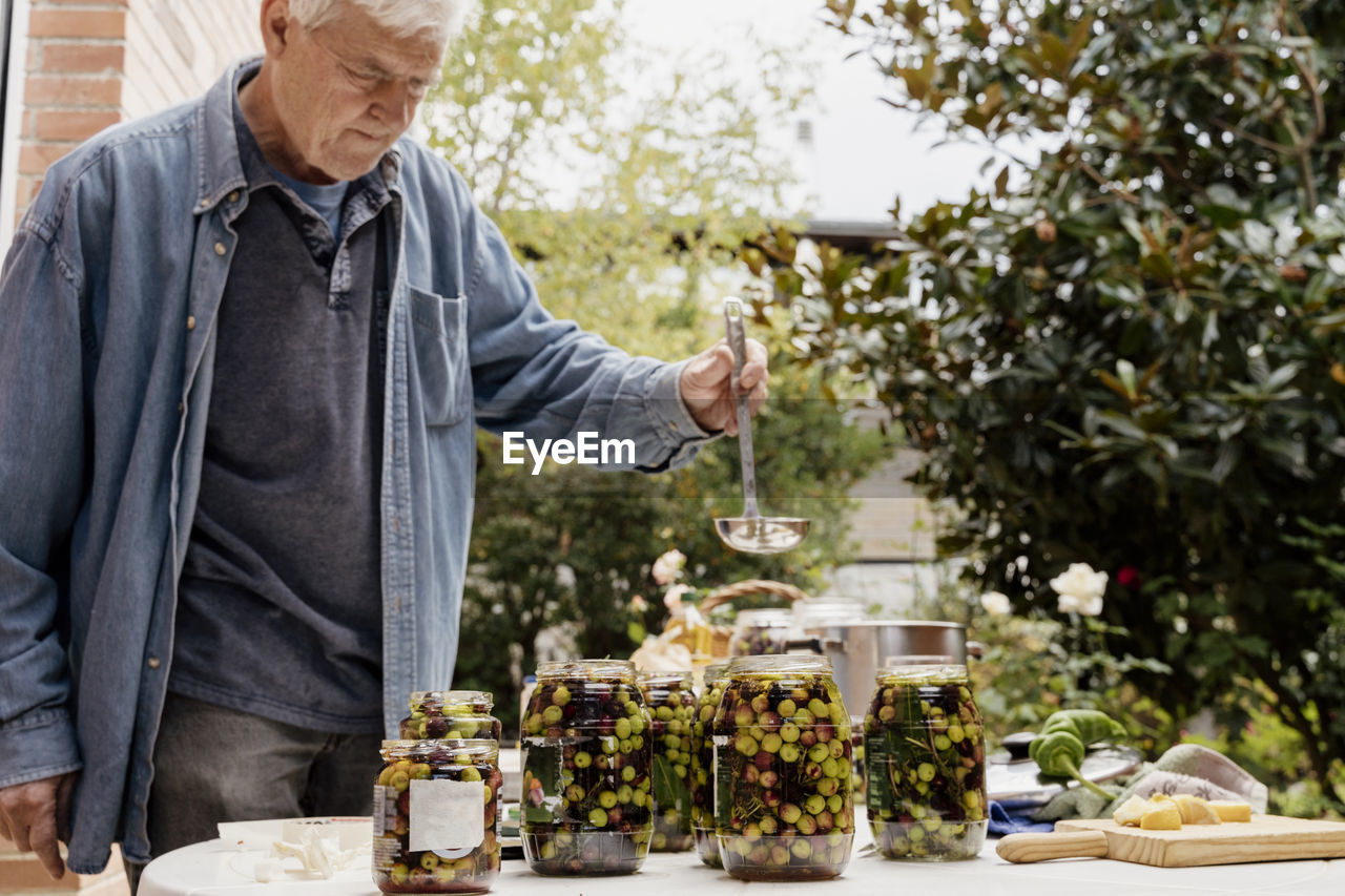 Senior man preparing olives in jars on table at back yard