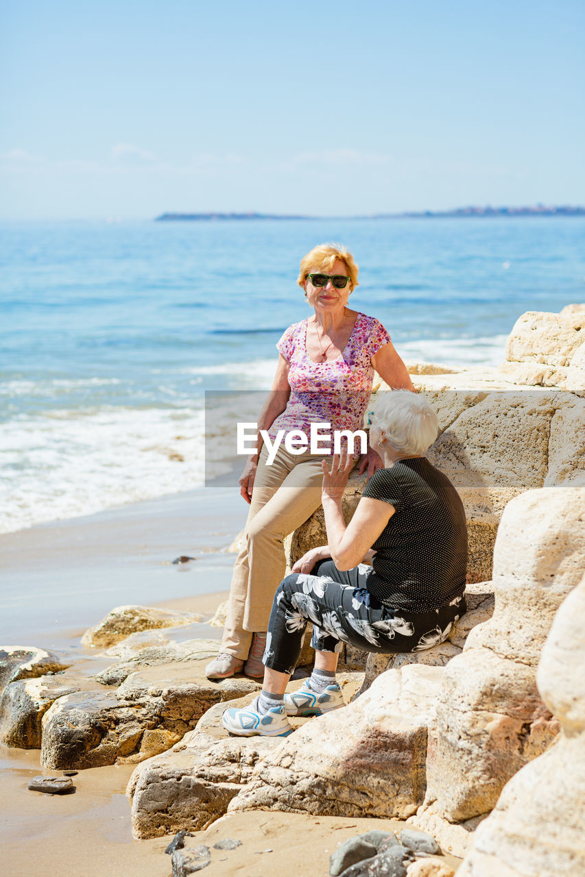 Two elderly women are happy to meet each other, sitting on a rock