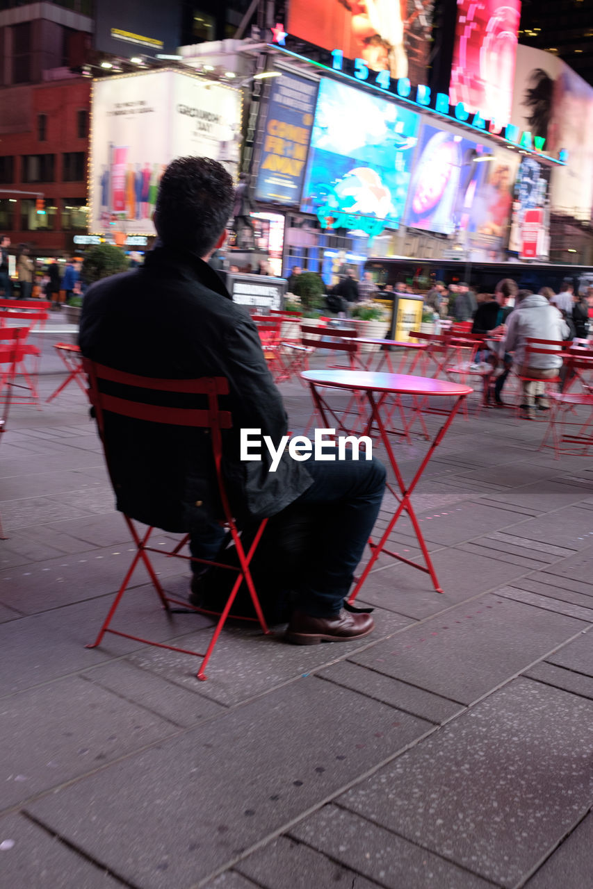 REAR VIEW OF MAN SITTING IN CITY