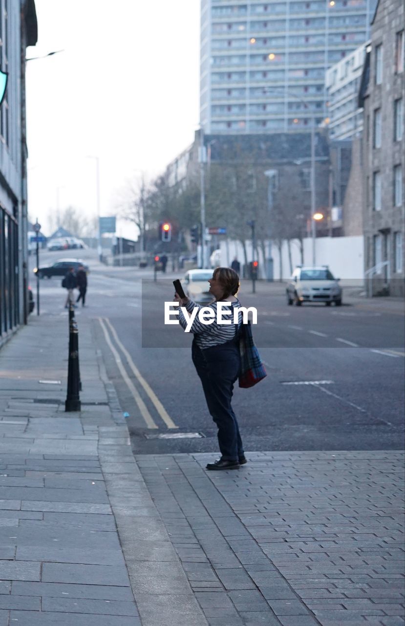 Side view of woman photographing on street in city