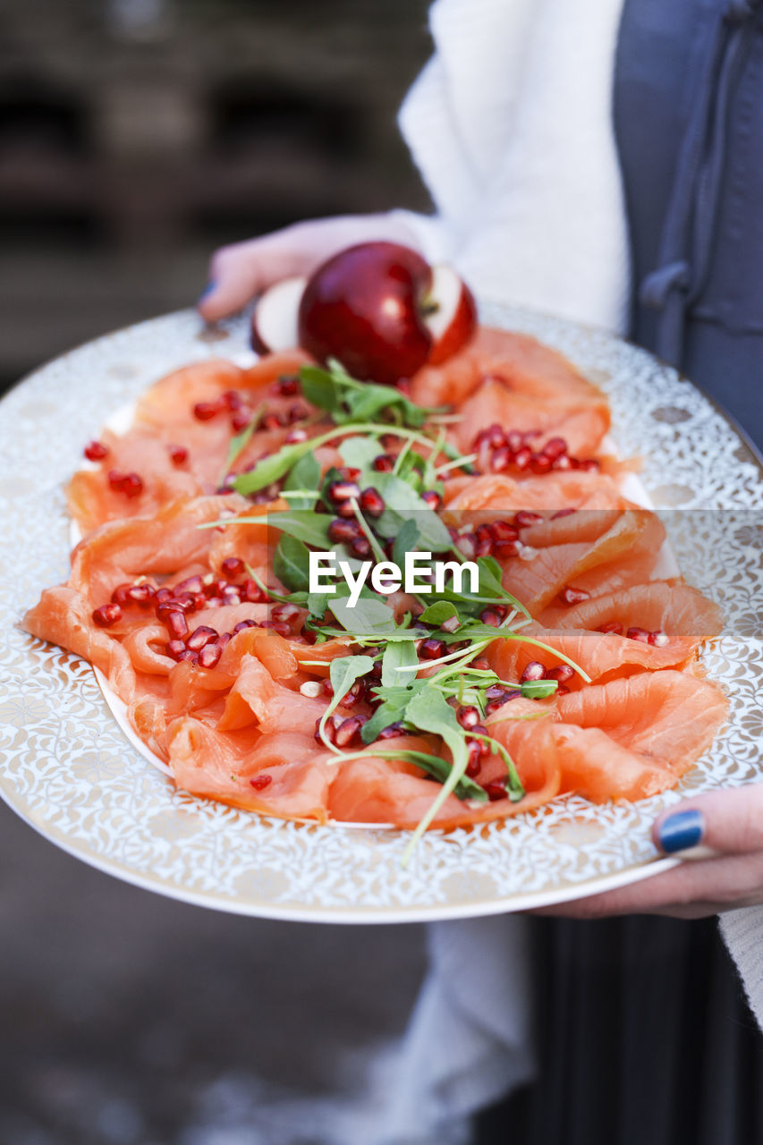 Person holding tray with smoked salmon and pomegranate seeds