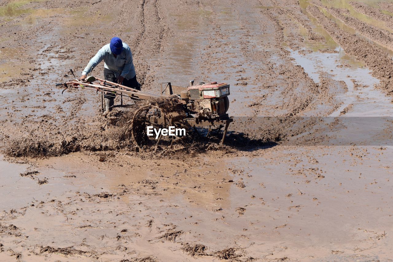 Man with agricultural machinery working on wet farm