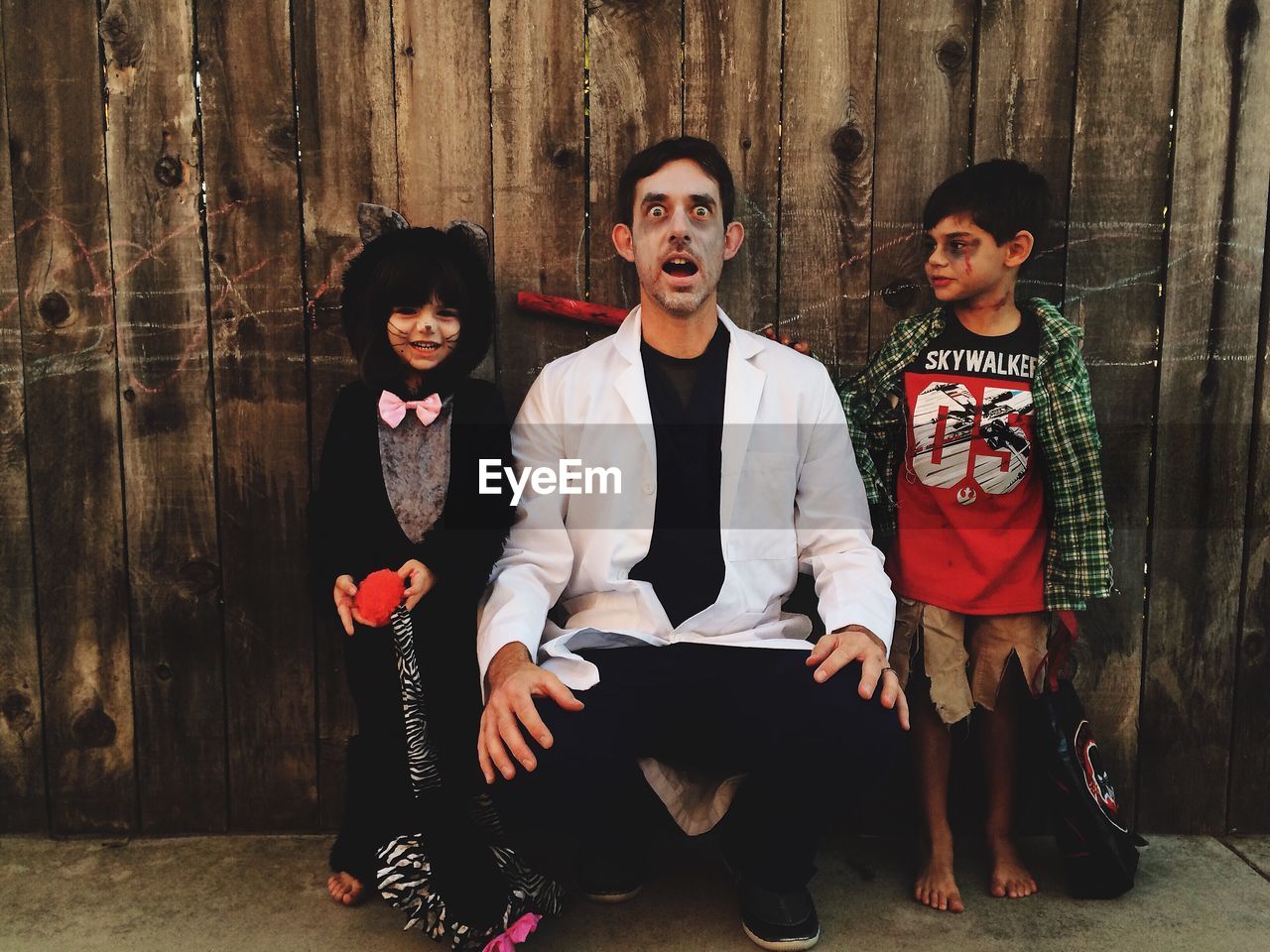Father with children in costume standing against wooden wall during halloween