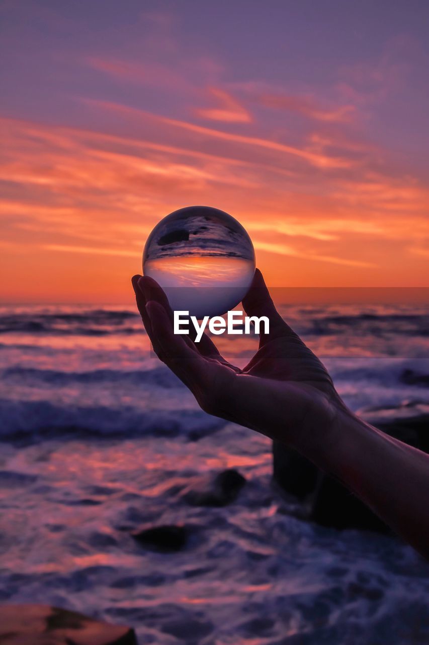 CLOSE-UP OF HAND HOLDING CRYSTAL BALL AGAINST SEA