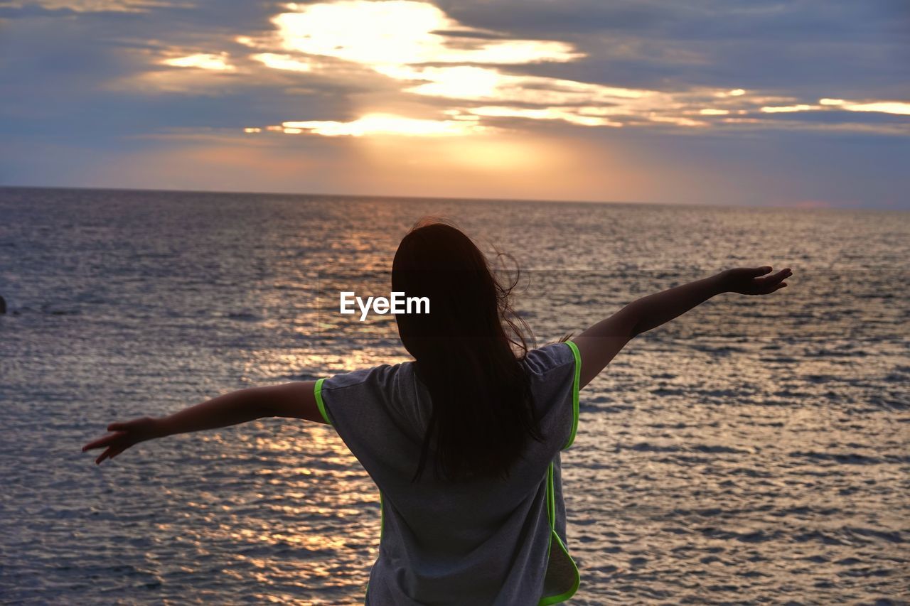 Woman standing at sea shore against sky during sunset