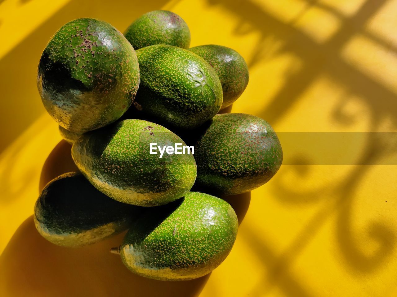 Close-up of avocado fruits pile up on yellow background with shadow