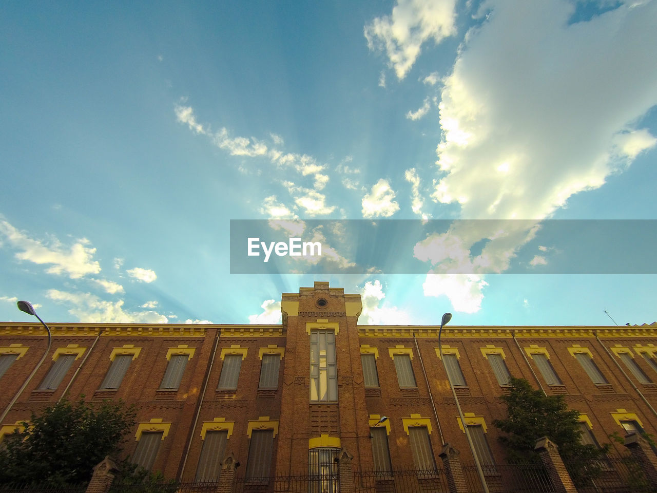 Low angle view of a brick building against the sunset light, with blue sky, clouds and sun rays. 