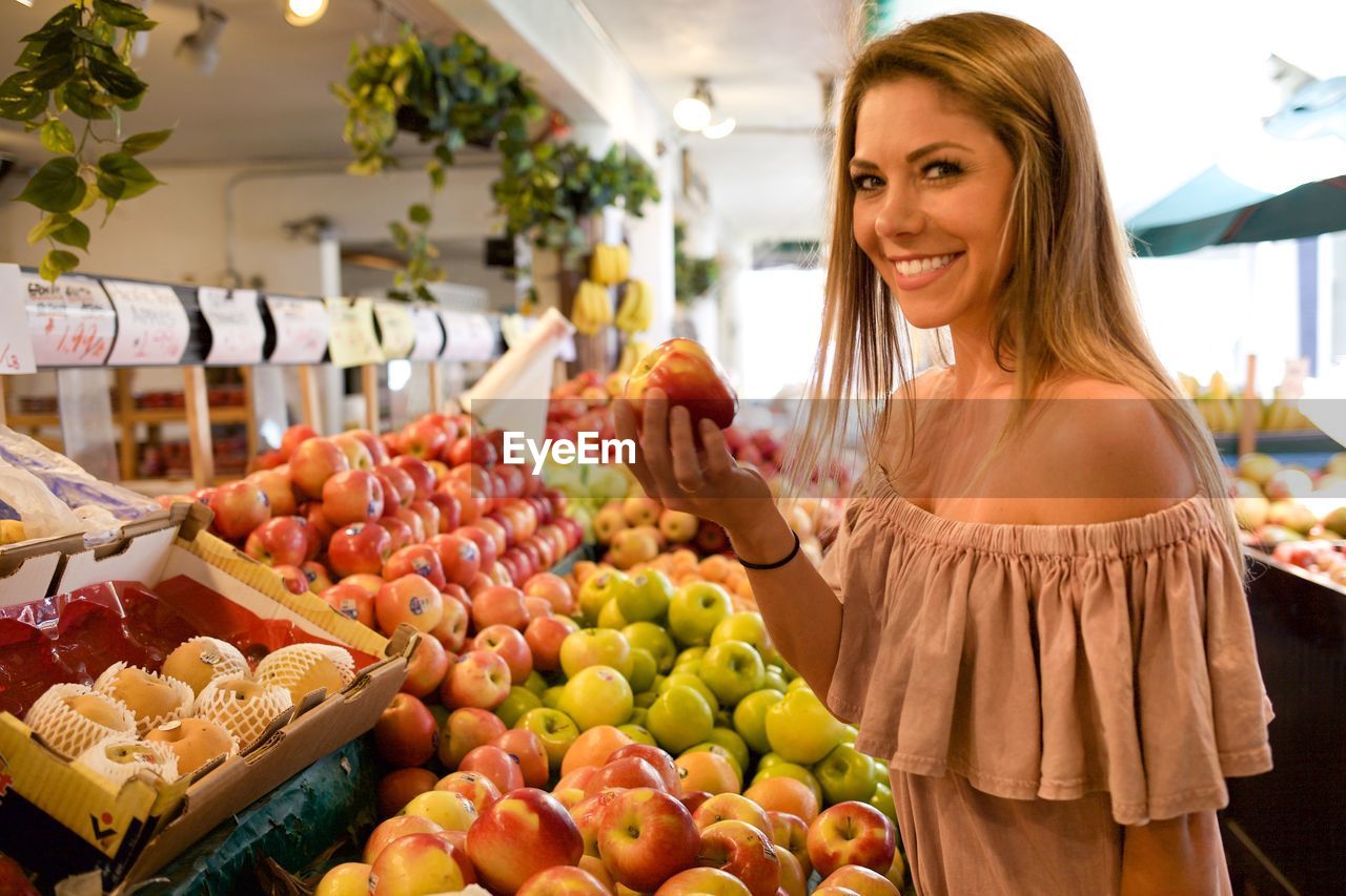 Side view portrait of beautiful woman smiling while buying apples in supermarket
