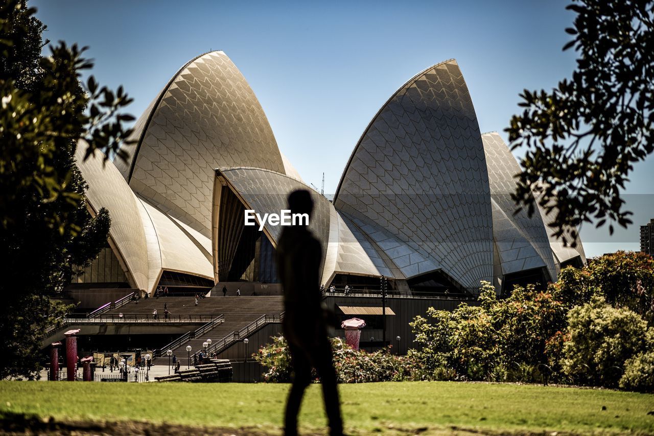 REAR VIEW OF MAN STANDING AGAINST BUILT STRUCTURE