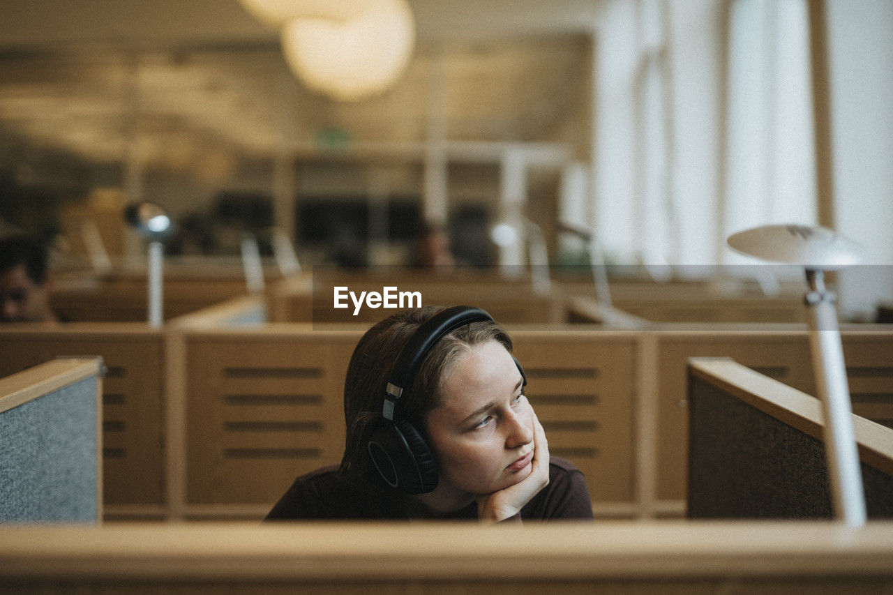 Contemplative young female student with hand on chin sitting in library at university