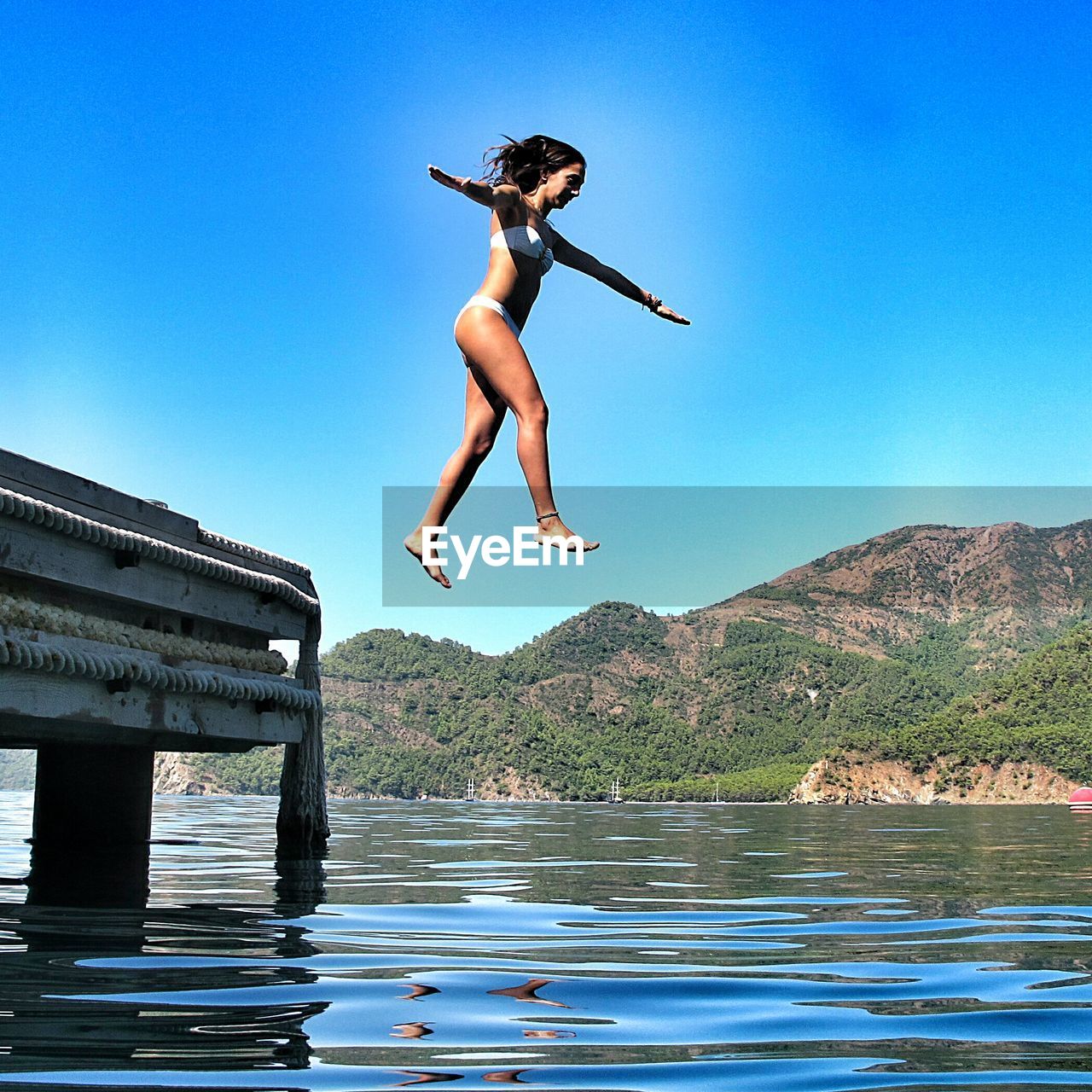 Full length of woman diving into lake against clear blue sky