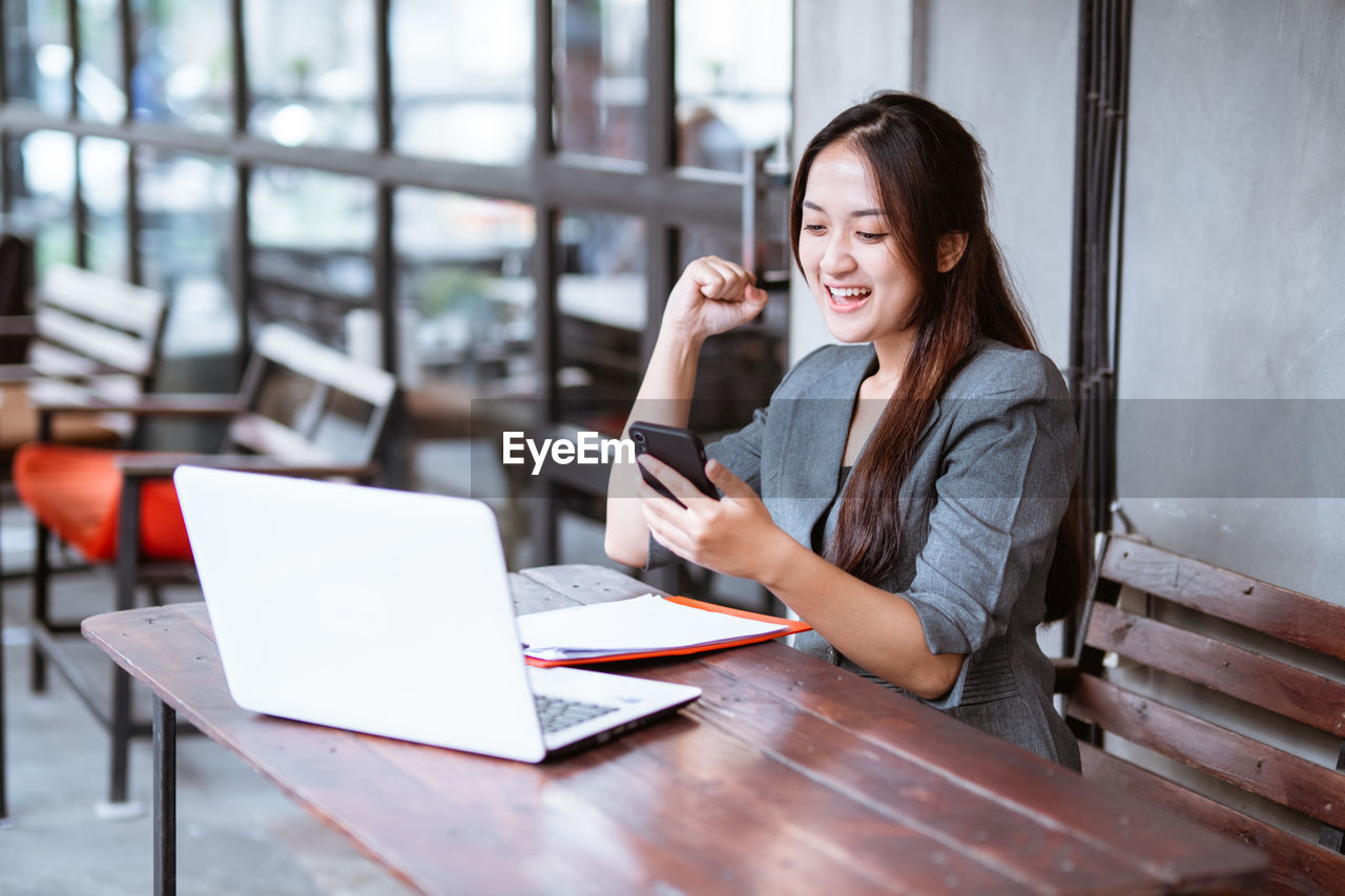 portrait of young woman using mobile phone while sitting at table