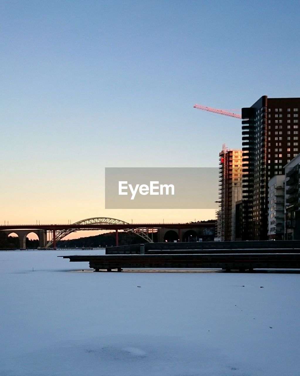 Bridge over frozen river by building against clear sky