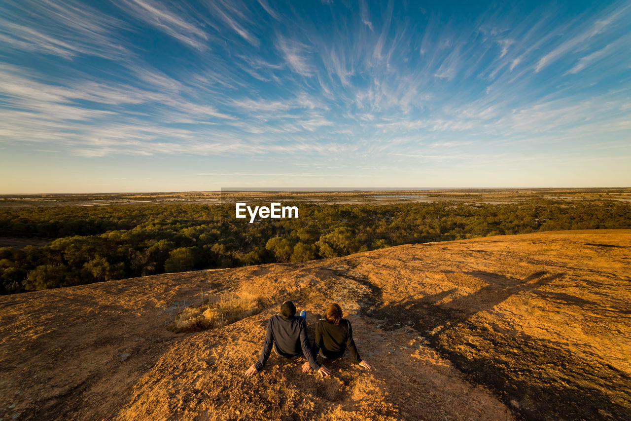 Rear view of couple sitting on mountain against sky