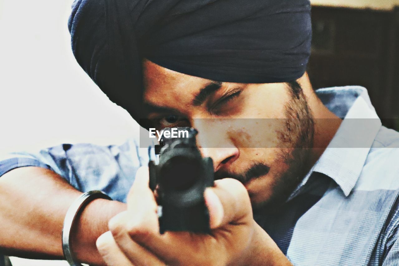 Close-up portrait of young man aiming with gun
