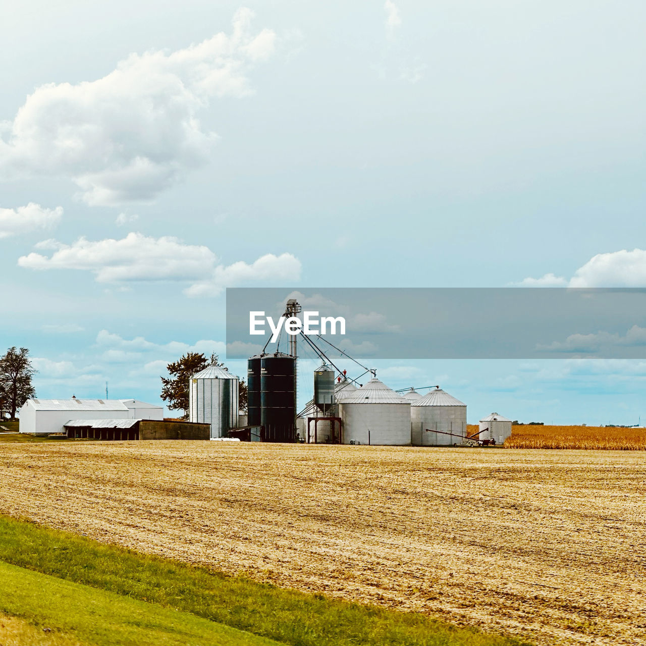 sky, agriculture, field, landscape, rural scene, cloud, farm, rural area, environment, land, nature, cereal plant, prairie, built structure, crop, architecture, day, machinery, plant, plain, horizon, no people, industry, harvesting, business finance and industry, silo, outdoors, building exterior, power generation, transportation, agricultural building, scenics - nature, agricultural machinery