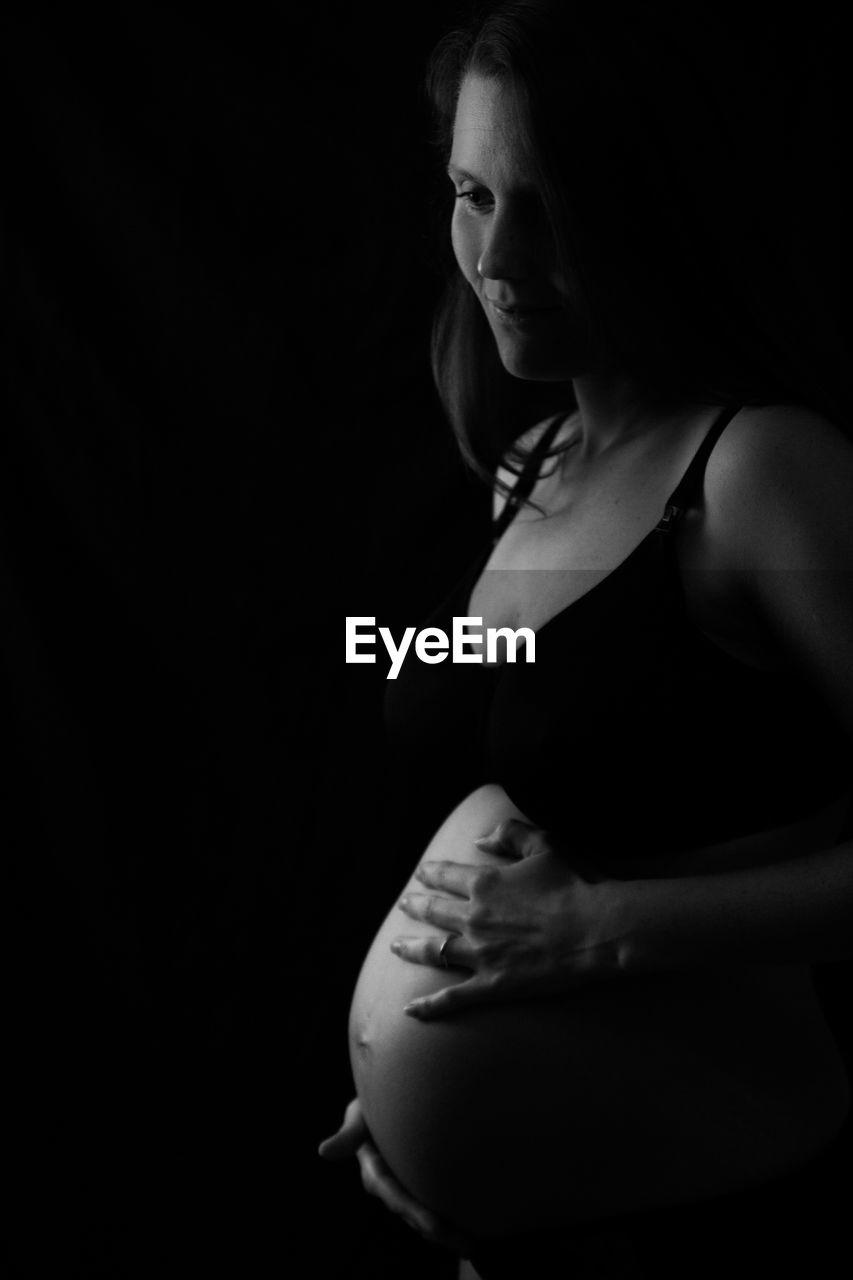 Smiling pregnant woman looking away while standing in darkroom