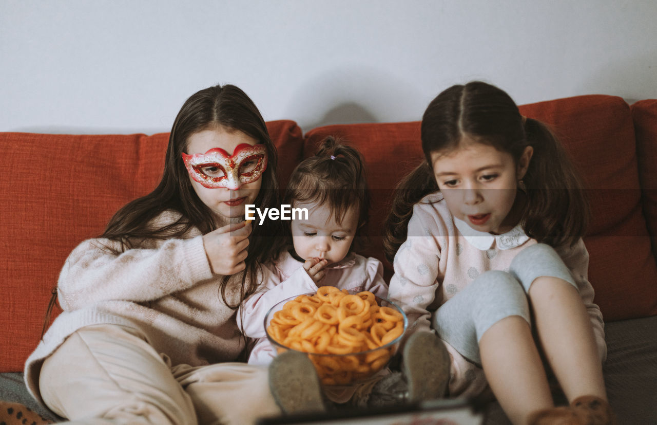 Three girls are watching a movie sitting on the couch.