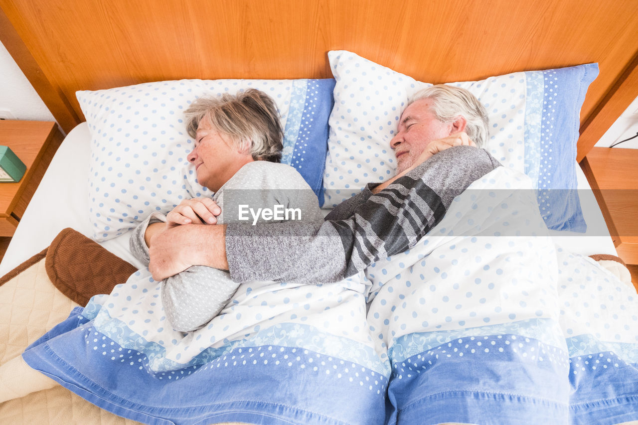 High angle view of senior couple sleeping on bed at home
