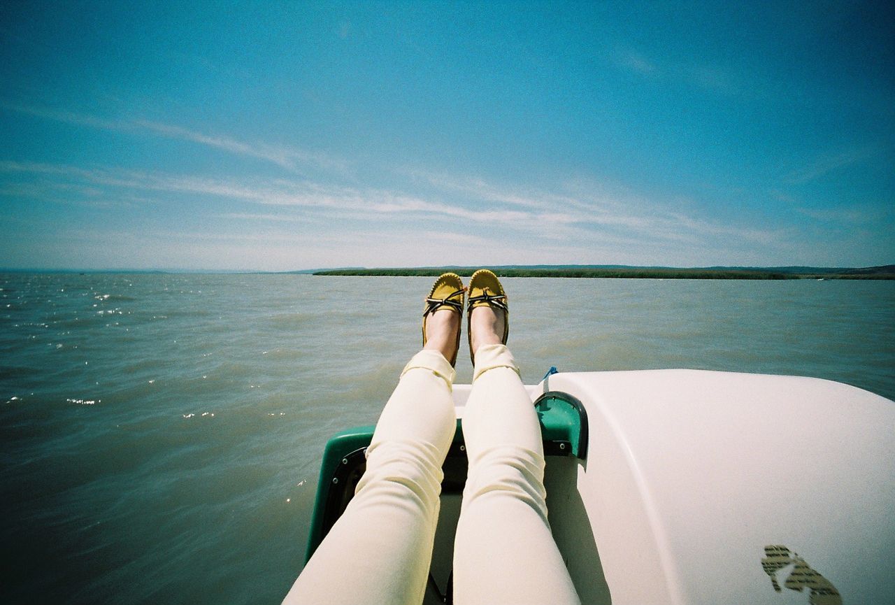 Low section of woman relaxing in pedal boat on lake against sky