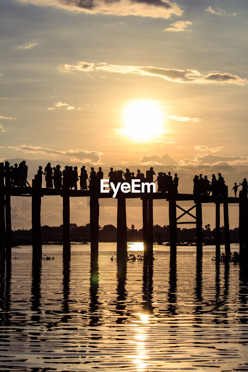 Silhouette people on pier over lake against sky during sunset