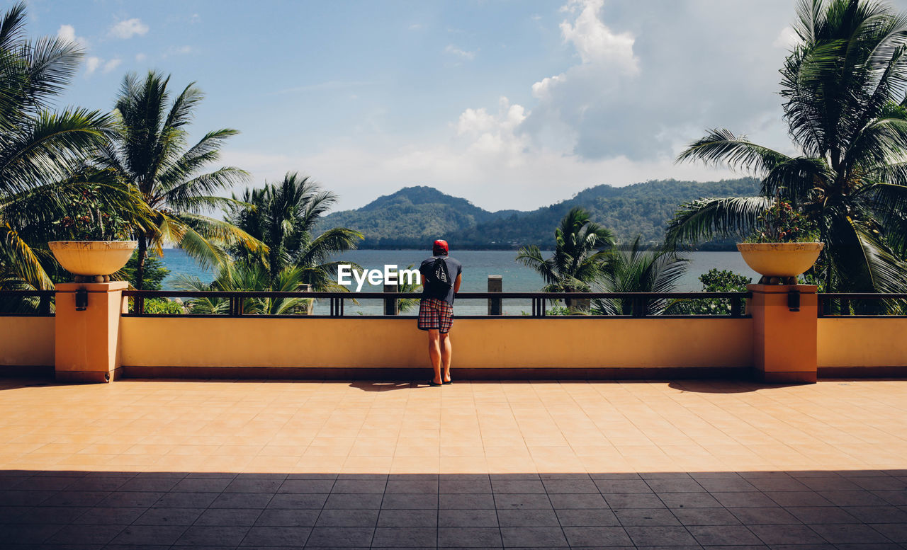 Rear view of man standing on walkway by sea against sky