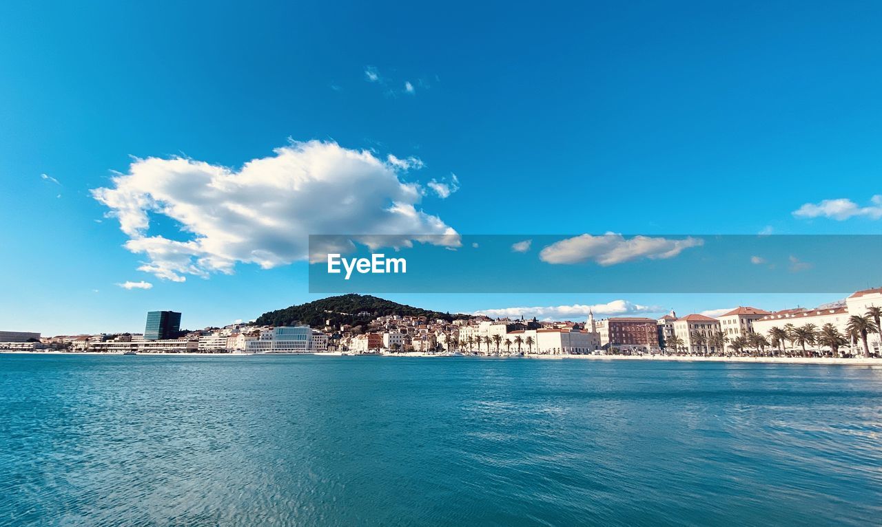 SCENIC VIEW OF SEA BY CITY BUILDINGS AGAINST BLUE SKY