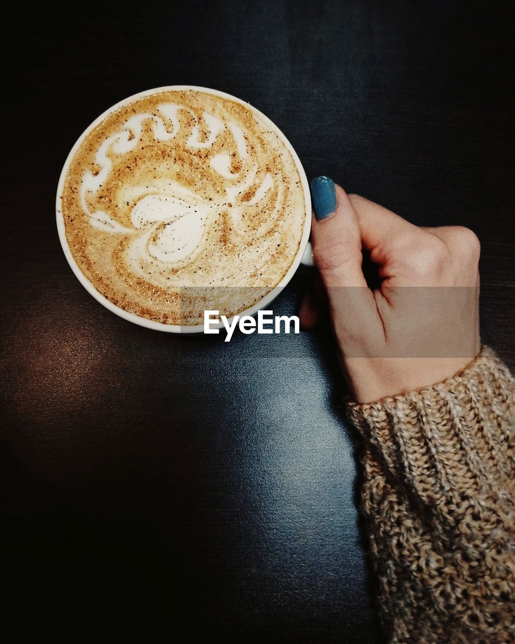 Cropped hand of woman holding coffee cup on table