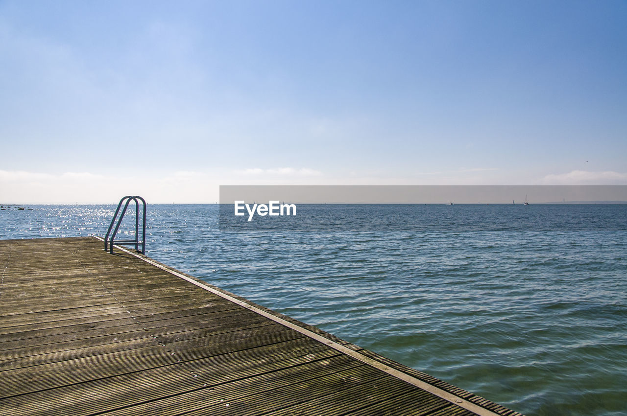 Scenic view of wooden deck with ladder by sea against sky