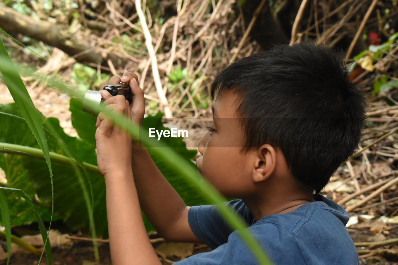 Side view of boy photographing plant in forest