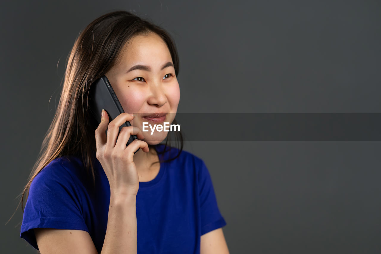 PORTRAIT OF BEAUTIFUL YOUNG WOMAN USING MOBILE PHONE WHILE STANDING ON CAMERA