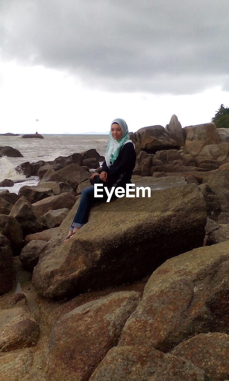 Portrait of woman sitting by sea on rock