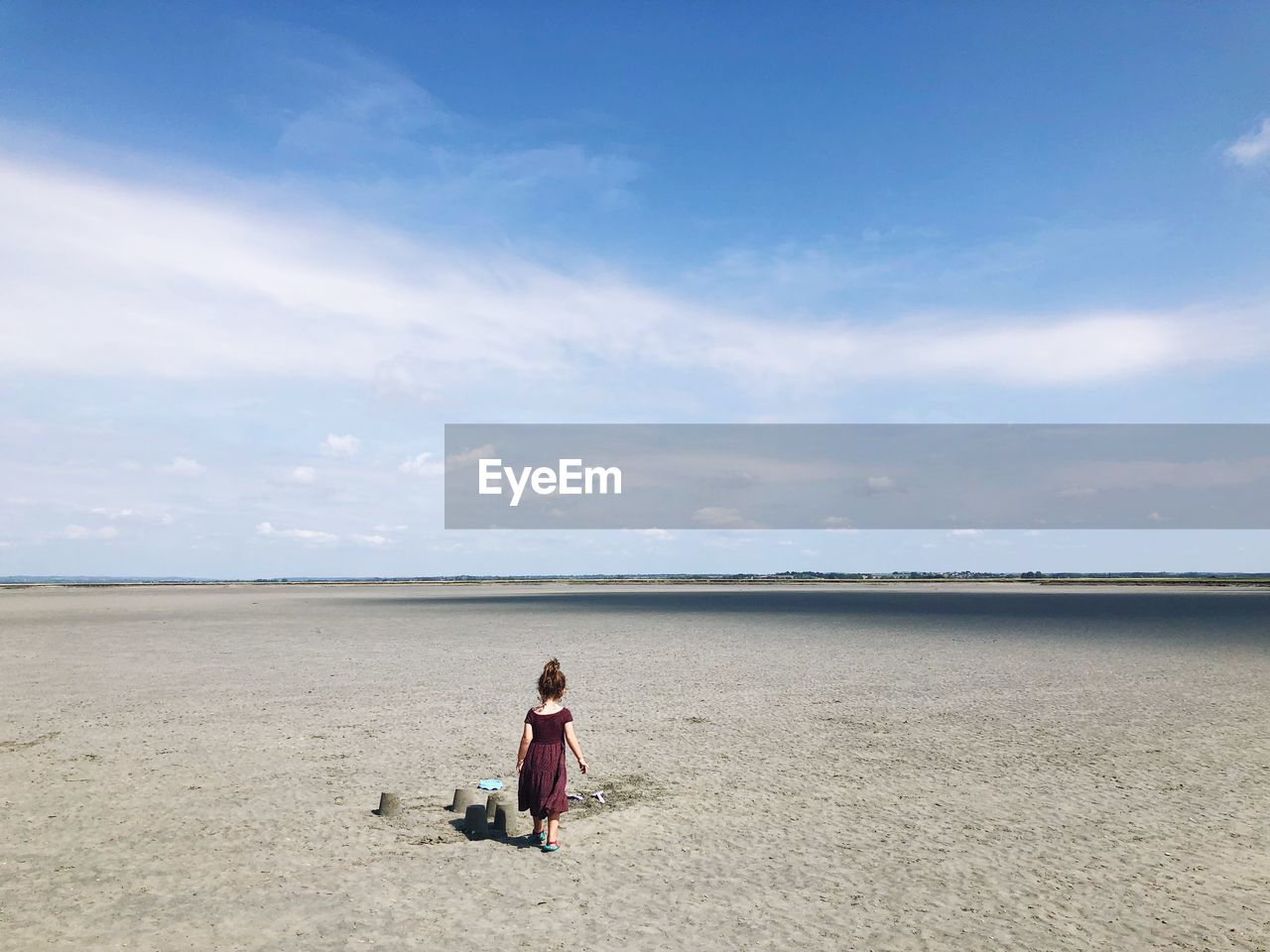 Rear view of girl walking by sandcastle at beach against sky