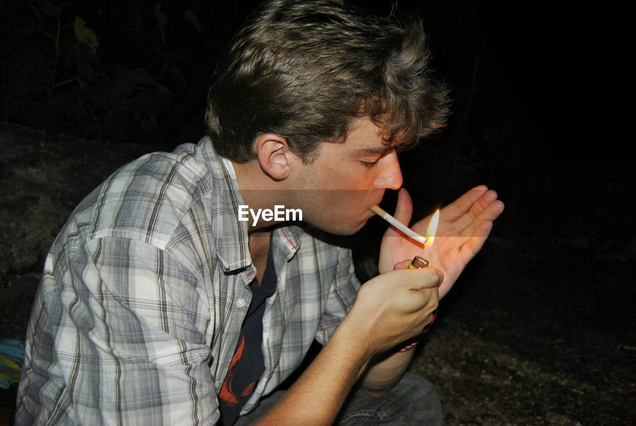 Young man burning cigarette at night