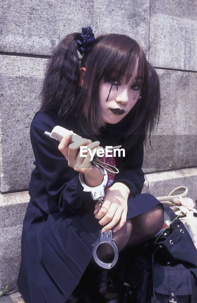 Young woman wearing make-up with handcuffs holding phone while sitting on steps