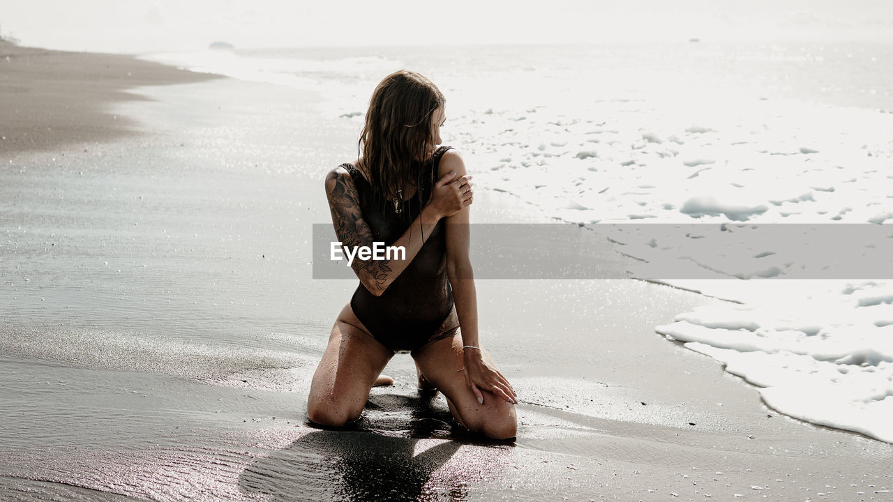 REAR VIEW OF WOMAN SITTING AT BEACH