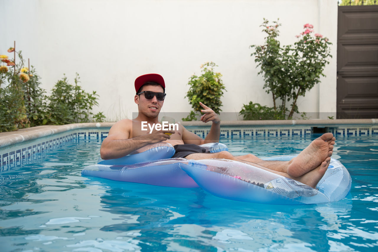 MAN RELAXING IN SWIMMING POOL AGAINST CLEAR SKY