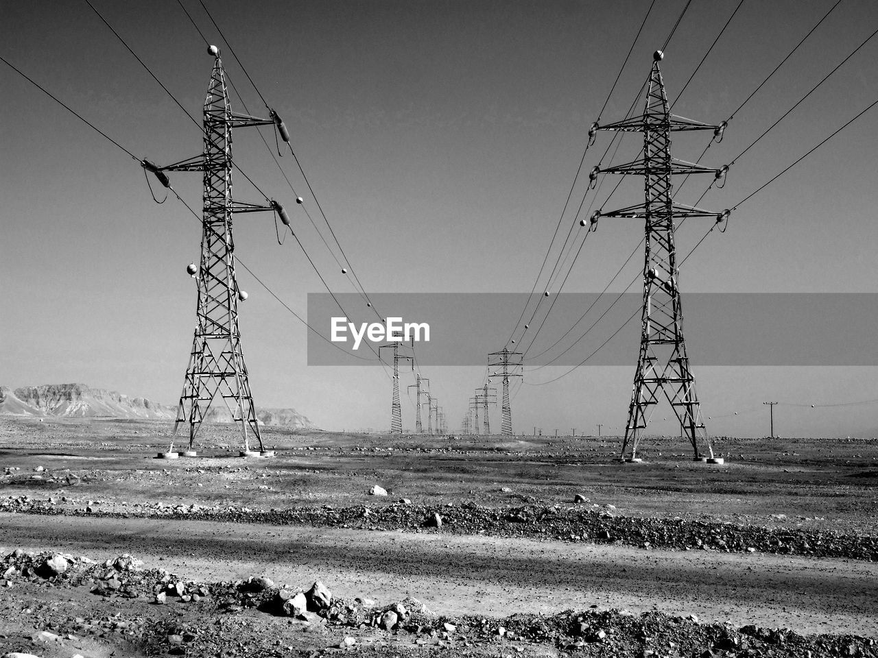 electricity, cable, electricity pylon, technology, black and white, power supply, power line, power generation, sky, transmission tower, nature, environment, landscape, monochrome photography, monochrome, land, tower, no people, overhead power line, field, day, rural scene, outdoors, agriculture, line, clear sky, scenics - nature, power cable, architecture, transportation