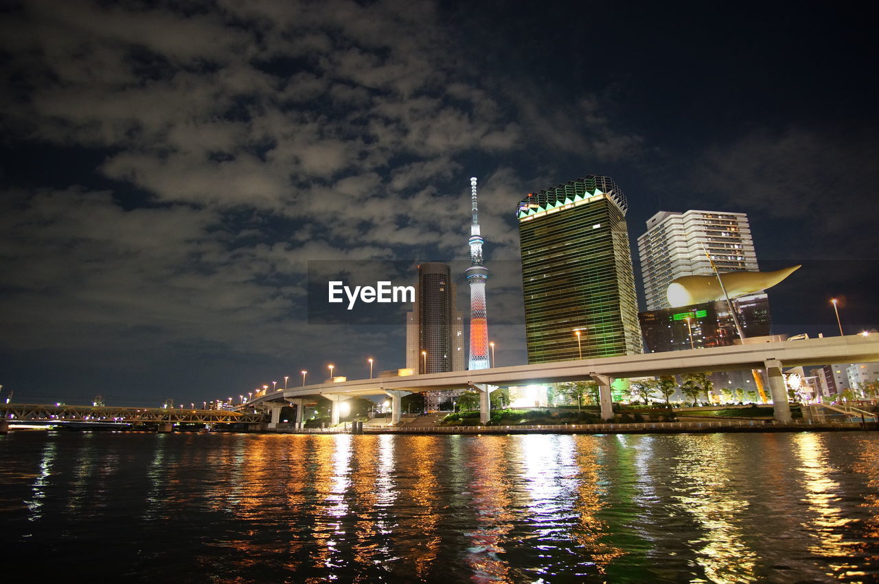 ILLUMINATED BUILDINGS BY RIVER AGAINST SKY