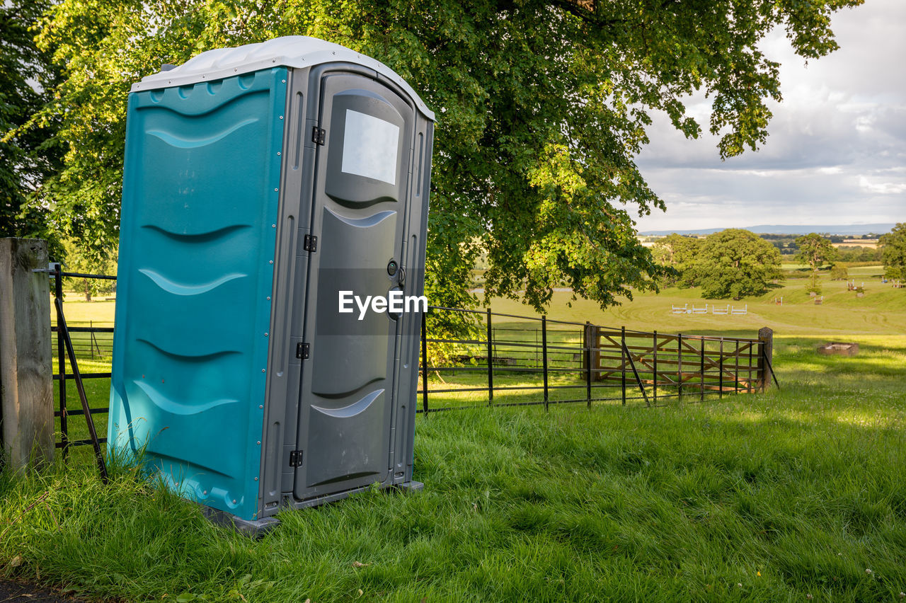 A plastic portable toilet in a field at an outdoor cross country horse trials event.