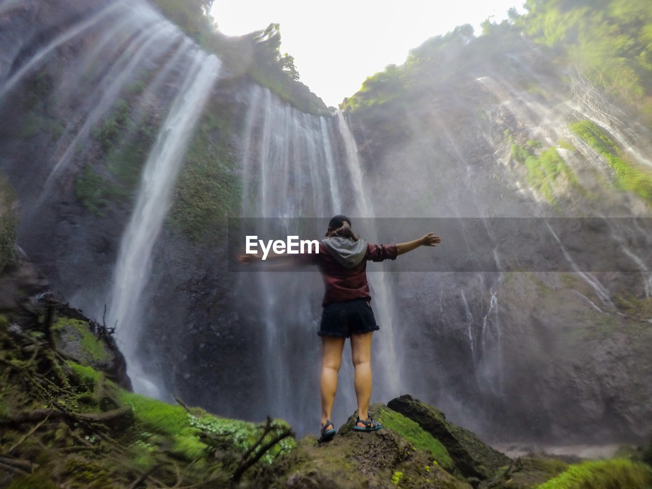 Blurred motion of woman outstretching in front of waterfall